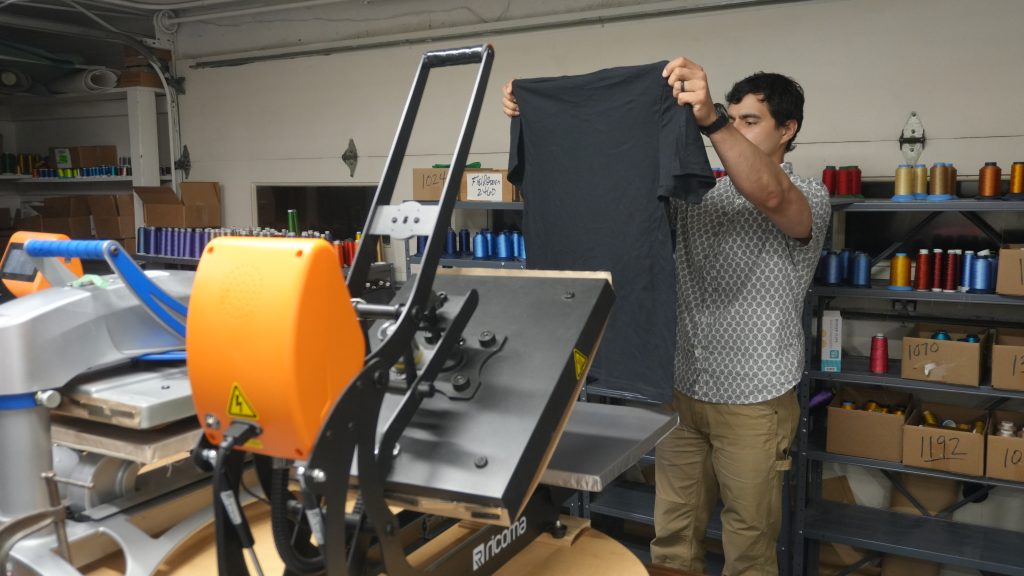 Jordan Gonzales inspecting custom printed apparel in the Generation Embroidery shop